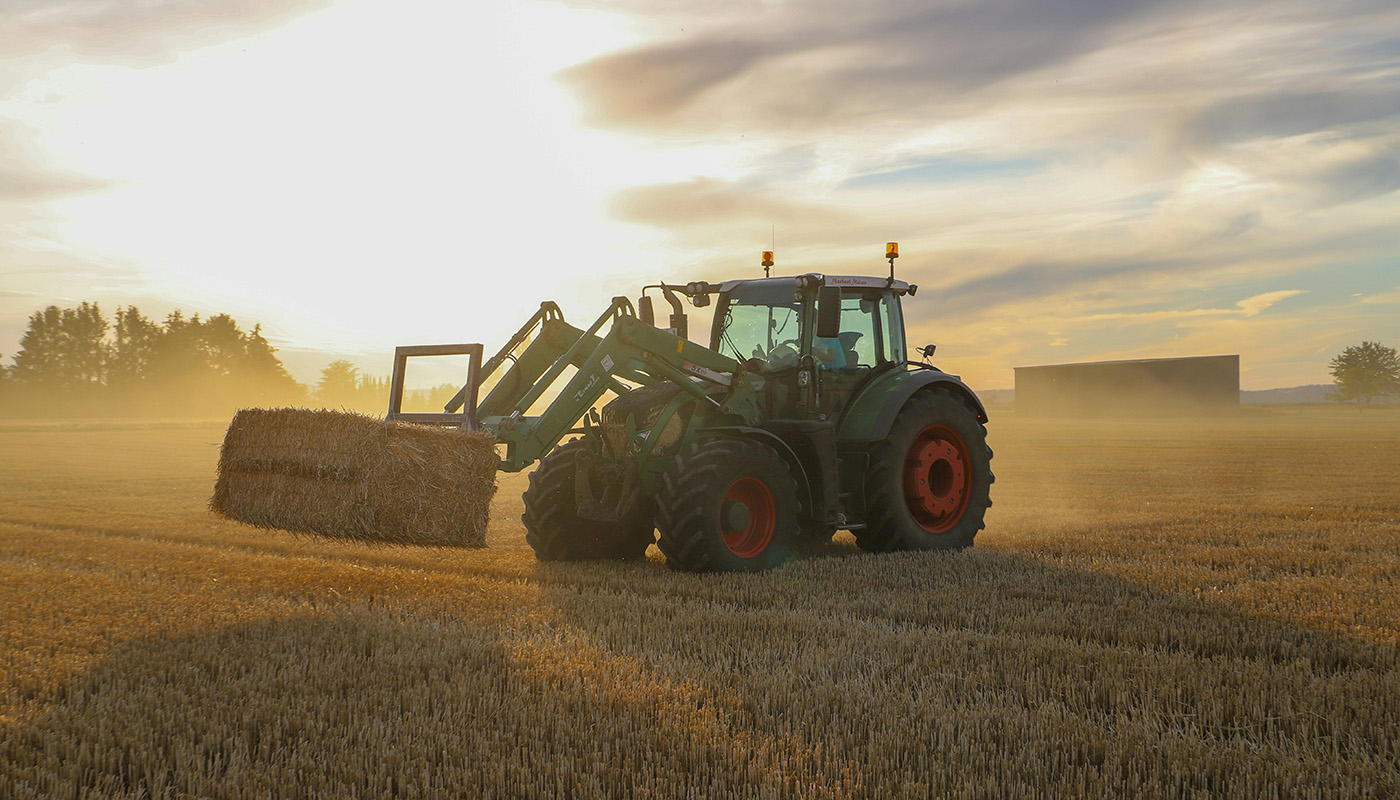 Man using tractor to move hay bundles.