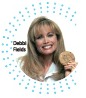 This is a photo of a person, likely a woman, who appears to be a public figure or celebrity, holding an award that says "Debi Fields." She is smiling and looking directly at the camera. The background is white with a circular blue and white pattern. The photo seems to be a headshot or promotional image for the award.