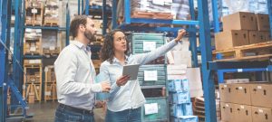 Two people standing in a large, well-stocked warehouse.