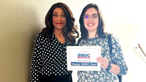 Two people standing together, holding a paper with a message. The person on the right is smiling and holding a paper with the text "Happy 85th SBD."