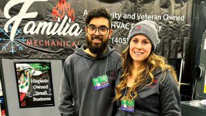 A couple in a booth at a convention, smiling and posing.