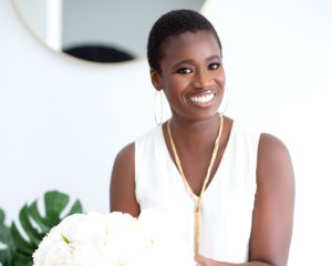 A person is smiling, holding a bouquet of flowers in front of them.