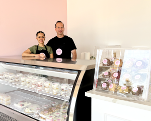 A couple stands in front of a bakery counter filled with desserts.