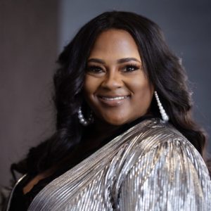 This image shows a woman posing for a photo wearing a silver cardigan and a black shirt
