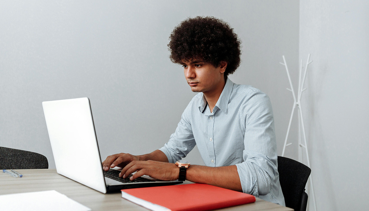 A woman with curly hair smiles while talking on her phone and using a laptop at a wooden table in a bright, cozy room.