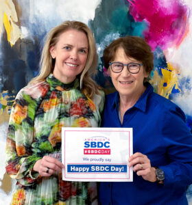 Two women smiling holding a sign with "Happy SBDC Day!" on it.